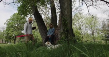 Köpekleri ile birlikte büyük bir ağacın altında sohbet ve kahveden zevk alan çiftler..