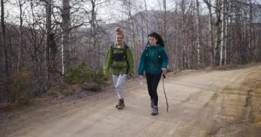 İki bayan arkadaş dağlardaki toprak yolda yürüyüş yapmaktan zevk alıyor. Sırt çantaları, yürüyüş botları ve baston taşıyorlar..