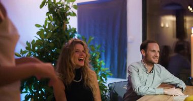 Arkadaşlar akşam yemeği için toplanır. Genç bir kadın, dinleyen ve gülen arkadaşlarına kadeh kaldırır..