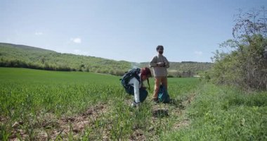Tarlalarda yürüyüş yapan, mola veren, vites ayarlayan bir çift. Güneşli yaz gününde doğadaki yeşil tarlalar ve ormanlar.