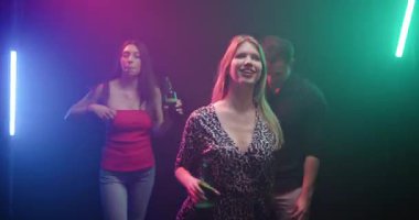 Genç yetişkinler neon ışıklı ve dumanlı bir partide dans edip içiyorlar. Atmosfer enerjik, eğlenceli ve heyecan verici. Gençlik ruhunu yansıtıyor..