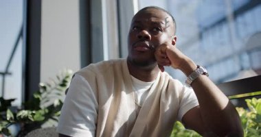 Düşünceli bir adam pencerenin kenarında oturur, beklerken şehri seyreder, dalgın dalgın dalgın dalgın. Güneş ışığı içeri giriyor, sahneyi aydınlatıyor ve şık kıyafetlerini aydınlatıyor..