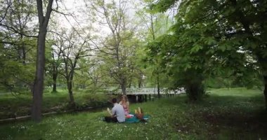 Çift nehir kenarındaki parkta romantik bir pikniğin tadını çıkarıyor. Etrafları yemyeşil ve ağaçlarla çevrili. Huzurlu ve huzurlu bir atmosfer yaratıyorlar..