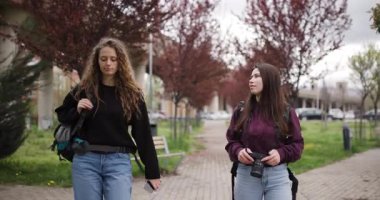 Sırt çantalı ve kameralı iki genç kadın parkta yürüyüp konuşuyor. Seyahat planlarını tartışıp telefondaki haritaya bakıyorlar..