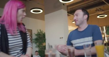 Pembe saçlı bir kız bir kafede bir arkadaşıyla gülüyor. Sıcak bir masada oturuyorlar, içkiler etrafa yayılmış, öğleden sonraki ışıkta canlı bir tartışmanın tadını çıkarıyorlar..