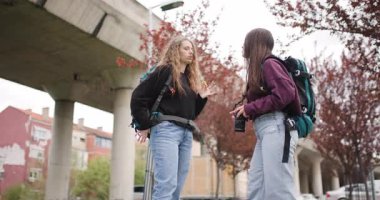 Sırt çantalı ve kameralı iki genç kadın fotoğraflara bakıyor ve şehirde selfie çekiyorlar..