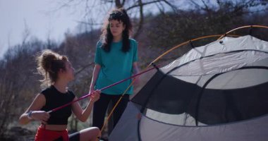 İki bayan arkadaş çölde bir nehrin kenarında çadır kuruyorlar. Kutupları birleştirip kamp kurma sürecini tartışıyorlar..