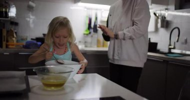 Genç bir kız, anne ve babasının mutfaktaki bir kasede malzemeleri karıştırmasına yardım eder. Birlikte yemek tarifi hazırlıyorlar..