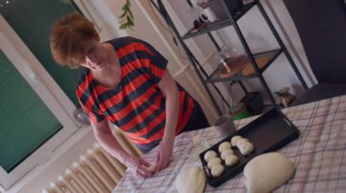 Yaşlı bir kadın sıcak mutfağında ev yapımı rulo yapıyor. Hamuru ustalıkla şekillendirir ve düzenler, pişirmeye hazırdır..