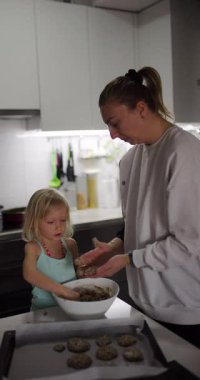 Anne ve kızı modern bir mutfakta birlikte sağlıklı kurabiyeler yapıyorlar. Kurabiye hamurundan küçük toplar yapıp tavaya koyuyorlar..