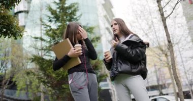 Üniversite kampüsünde sohbet edip kahve içen iki genç kız.