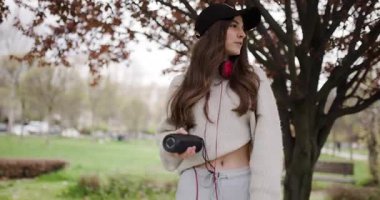 Tasasız Genç Kız Parkta Müzikten Hoşlanıyor, Kulaklık takıyor ve Bir Ağacın Altında Portatif Hoparlör Tutuyor