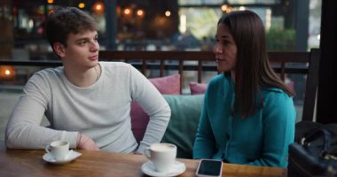 İki genç, erkek ve kadın, bir kafede kahve içip sohbet ediyorlar. Gülümsüyorlar ve mutlular.