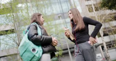 İki genç kız sohbet ediyor ve liselerinin ya da kampüslerinin yakınında kahve içiyor, cep telefonunda bir konuyu tartışıyorlar.