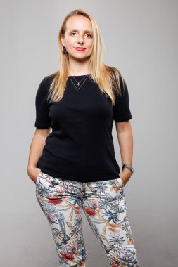 Kendine güvenen bir iş kadını elleri ceplerinde şık bir siyah bluz ve çiçekli pantolon giyer. Rahat tavrı profesyonelliğini ve modern moda anlayışını vurguluyor..