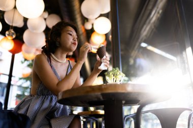 Genç bir kadın, bir kafede, sıcak ve davetkar bir ortam yaratan kağıt fenerlerle çevrili bir dondurma külahının tadını çıkarıyor..