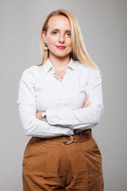 Kendine güvenen bir iş kadını kollarını kavuşturup beyaz gömlek ve taba rengi pantolon giyer. Rahat ama iddialı duruşu iş dünyasındaki profesyonelliğini ve kararlılığını yansıtıyor..