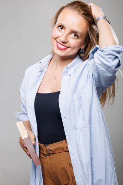 Bir iş kadını tarafsız bir stüdyo ortamında rahat bir şekilde duruyor, günlük kıyafetler giyiyor. Elinde kitap tutarken gülümsüyor, mesleki tavrını ve cana yakın kişiliğini yansıtıyor..