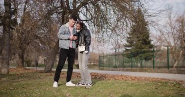 Genç bir çift parkta selfie çeker, beşlik çakar ve akıllı telefonlarına bakarken birlikte vakit geçirir..