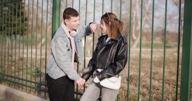 Genç bir çift çitin yanında durup el ele tutuşuyor, konuşuyor ve telefona bakıyor. Mutlular ve birbirlerine eşlik etmekten zevk alıyorlar..