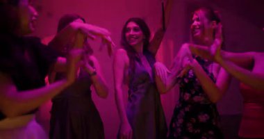 Şık parti elbiseleriyle beş kız arkadaş birlikte kutlama yapıyor, renkli neon ışıkların altında dans ediyor ve gülüyor, müzikten ve hareketli bir ev partisinde birbirlerine eşlik ediyorlar..