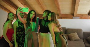 Mezuniyetlerini kutlayan bir grup arkadaş selfie çeker ve modern bir apartmandaki bir partide kutlama kadeh kaldırır..