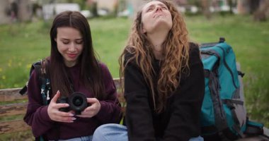 Parktaki bankta oturan iki genç kadın kameralarındaki fotoğraflara bakıp gülüyor ve konuşuyorlardı..