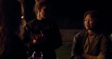 Üç arkadaş bir partide sohbet edip şarap içerek eğleniyorlar. Sıcak ışık ve rahat atmosfer bir yoldaşlık ve kutlama hissi yaratır..