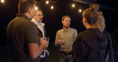 Arkadaşlar, açık hava toplantılarında içki içip sohbet etmekten zevk alıyorlar. Kahkahalar ve ışık altında güzel zamanlar.