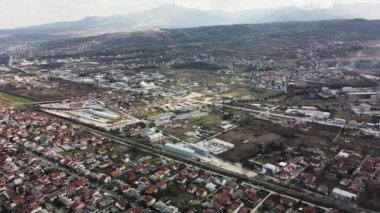 Aerial view of the industrial zone in Lisice, Skopje, North Macedonia, featuring factories, houses, roads, and mountains.