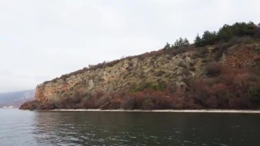 Rocky cliff shore with autumn trees at Lake Ohrid in North Macedonia. Scenic nature view of colorful forest and tranquil water.