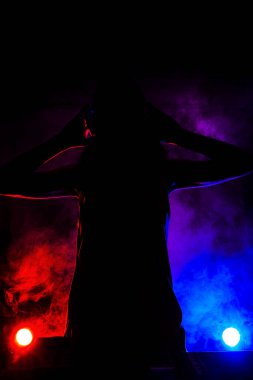 Silhouette of a girl DJ playing music on a mixer. Red and blue lights and smoke in the background
