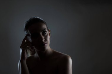 A dramatic portrait of a woman, cast in shadows, with a pensive look and moody illumination. Perfect capture of a contemplative mood in low light.