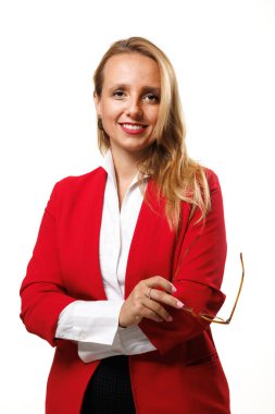 A businesswoman stands confidently, wearing a vibrant red blazer and a white blouse. With a friendly smile, she holds her glasses, showcasing her professional demeanor in a well-lit studio.
