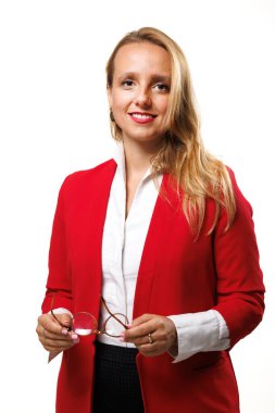 A confident businesswoman stands in a studio, wearing a striking red blazer and holding glasses. Her professional demeanor and warm smile reflect a successful career in business.