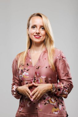 A businesswoman stands confidently in a trendy blouse, engaging the audience with her poised demeanor. The backdrop is a plain, neutral color, emphasizing her professionalism during a discussion.