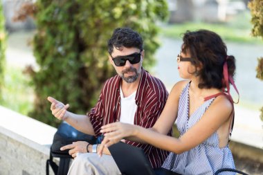 Two individuals having a lively conversation outside in a park. They appear relaxed and engaged in their discussion.