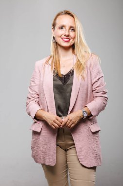 A businesswoman stands confidently with a slight smile, dressed in a stylish blazer and blouse. The neutral background highlights her professional look and approachable demeanor.