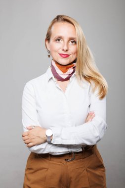 A poised lady stands confidently with arms crossed, wearing a stylish outfit and scarf. Her expression radiates professionalism and determination in a minimalist office environment.