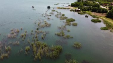 Aerial view of Lake Dojran in North Macedonia, showcasing reeds, tranquil waters, fishing huts, and the beautiful lakeside landscape.