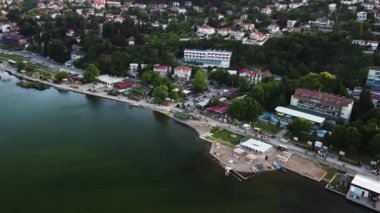 Aerial view of Lake Dojran, North Macedonia. The shoreline is dotted with hotels, restaurants, and shops. People are enjoying the lake on a summer evening.