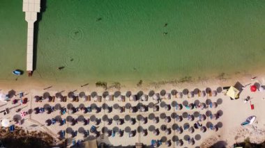 Tranquil aerial view of beach umbrellas, lounge chairs, and crystal-clear turquoise water. People enjoy swimming and sunbathing on a perfect summer day.
