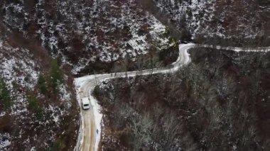 An SUV drives along a snowy dirt road through a valley in winter. This picturesque scene showcases the beauty of nature and adventure.
