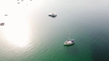 Sailboat and yacht at anchor in calm bay water. Sun reflecting on crystal-clear turquoise water. Small boats anchored near the beach. Ammouliani Island, Greece.