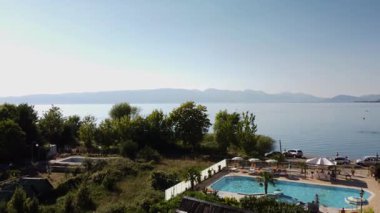 Construction site overlooking Lake Ohrid in North Macedonia. The serene view of the lake and mountains contrasts with the unfinished concrete structure.