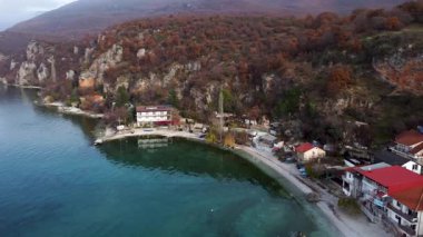 Scenic aerial view of Trpejca village on Lake Ohrid in North Macedonia during autumn. The tranquil waters reflect the colorful foliage along the shoreline.