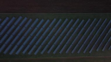 Aerial view of a solar panel farm at dusk. The panels are arranged in neat rows, and the surrounding landscape is visible.