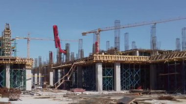 Workers are busy at a construction site, assembling steel structures and using cranes. Concrete is being poured, highlighting the ongoing development of a large commercial project.