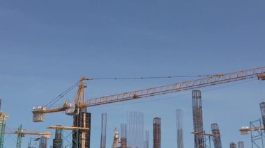 Workers are busy at a construction site under a clear blue sky. Cranes lift materials while scaffolding supports the buildings progress during the warm afternoon hours.