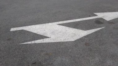 White arrow painted on asphalt road surface. Video shows a weathered directional arrow marking.